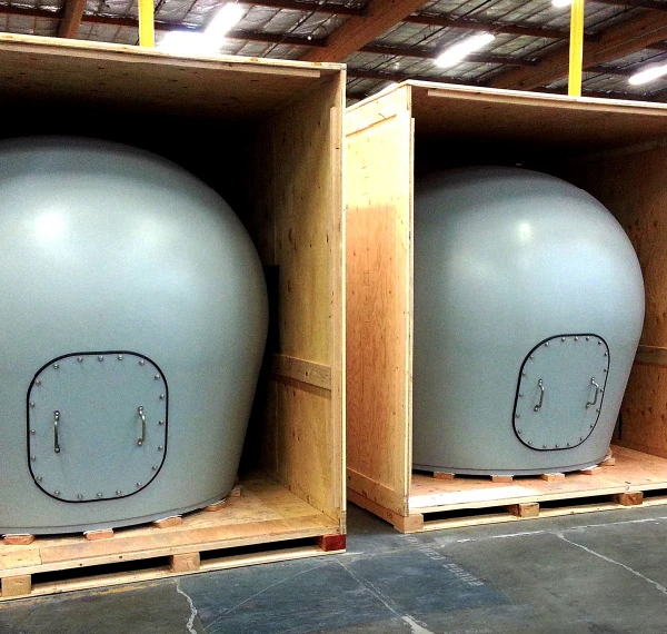 Two large, gray, dome-shaped radomes with bolted doors sit inside open wooden crates on a warehouse floor, clearly visible.